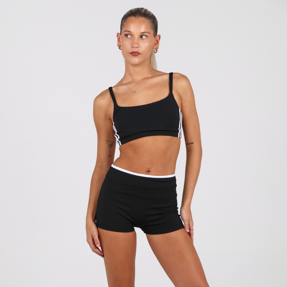 Woman wearing a black sports bra and shorts set on a plain background